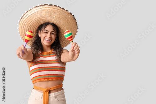 Happy young African-American woman in sombrero hat with maracas on grey backg...