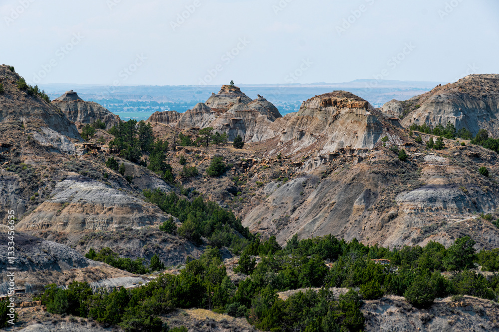 Naklejka premium An expansive view of dramatic badlands showcases rugged hills, layered rock formations, and patches of greenery, depicting the beauty of nature's artistry.