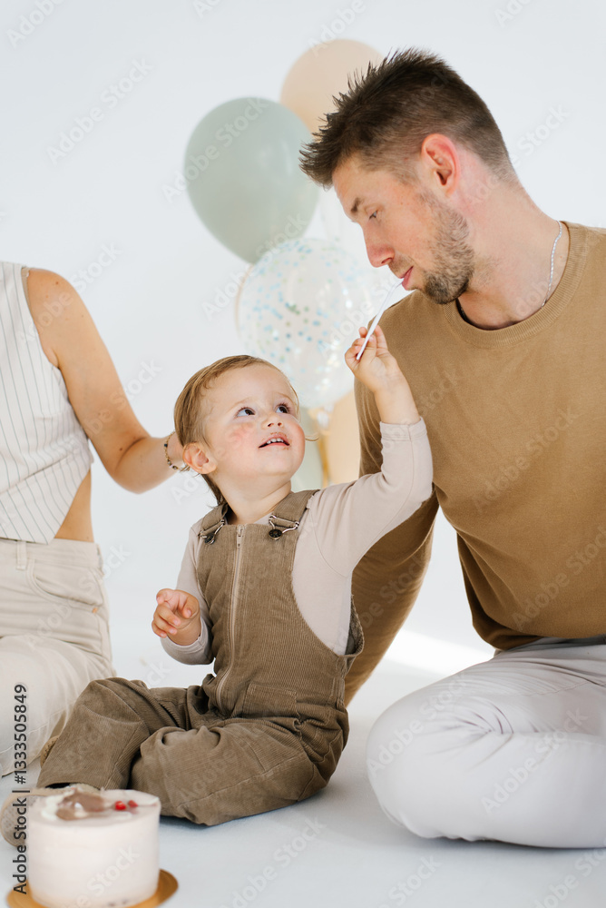 Happy parents with their birthday son are sitting on the floor near the cake, the boy treats his father with a piece of sweet