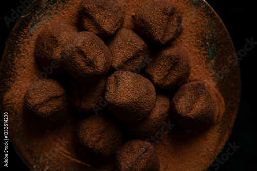 Overhead view of artisanal chocolate truffles heavily dusted with dark cocoa powder on a rustic plate and dark
background