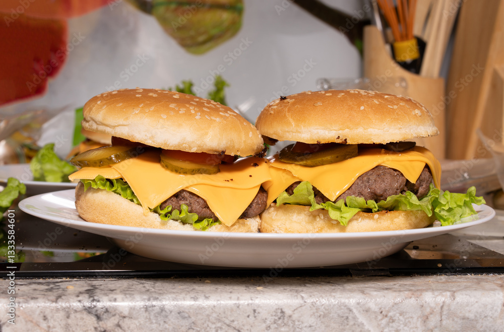Two cheeseburgers with sesame buns, beef patties, melted cheddar, lettuce, pickles, and tomato sit on a white plate, ready for serving.