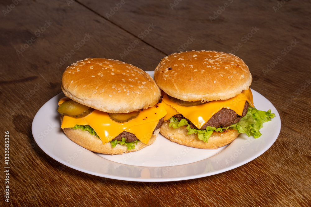 Two cheeseburgers with beef patties, melted cheese, lettuce, and pickles on sesame buns, served on a white plate atop a rustic wooden surface.