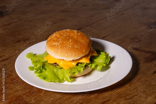 Obraz na płótnie A juicy cheeseburger with a sesame seed bun, melted cheese, beef patty, and lettuce on a white plate, styled atop a rustic wooden background. w salonie