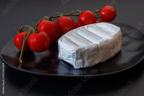 Soft brie cheese with fresh cherry tomatoes on a black plate
