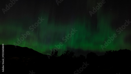 The majestic green lights of the Aurora Borealis dance gracefully over the horizon, casting a stunning glow that captivates viewers and elevates the night sky's beauty.
