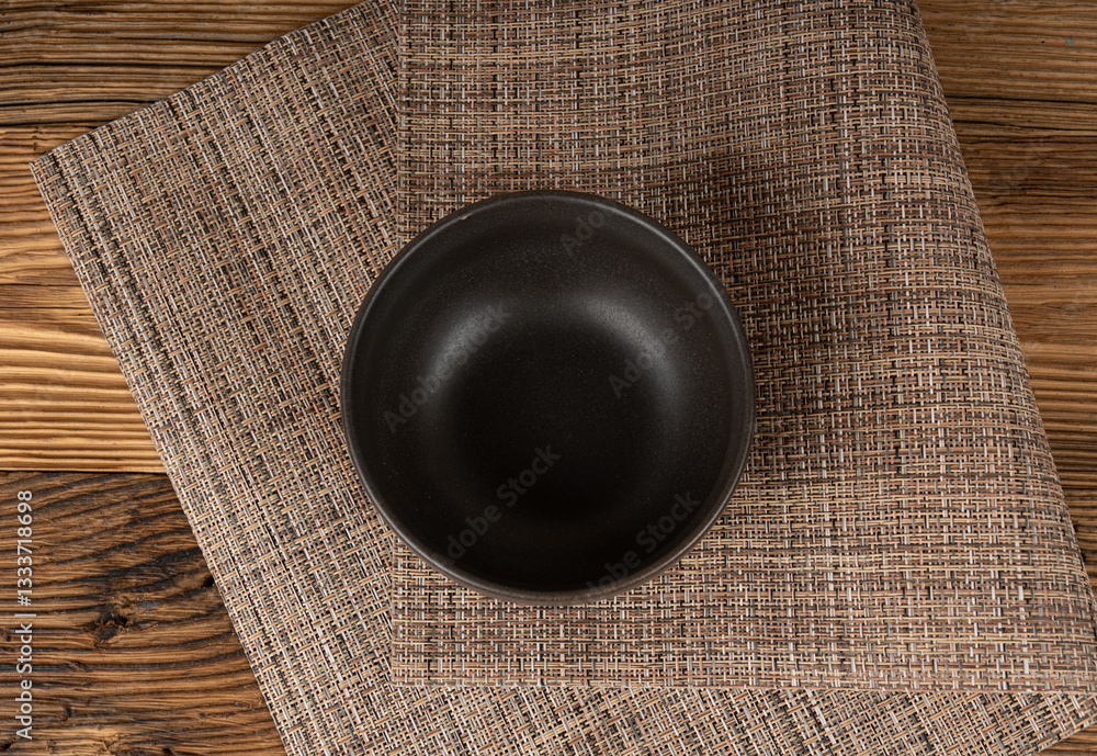 Fototapeta premium Empty bowl on table, black plate on wooden table and grey tablecloth, dark porcelain dish mockup
