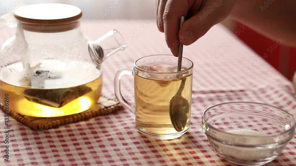 A man's hand stirs sugar in a glass mug with green herbal hot tea. A man's hand stirs sugar in a glass mug with green herbal hot tea.