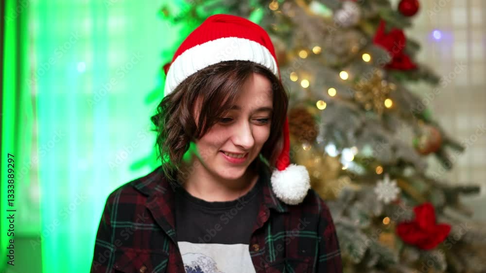 Good-looking happy Caucasian lady working at laptop. Brunette wearing Santa cap communicating online. Christmas tree at backdrop. Good-looking happy Caucasian lady working at laptop. Brunette wearing Santa cap communicating online. Christmas tree at backdrop.