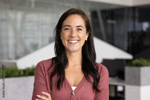 Cheerful beautiful Latin business leader woman looking at camera, keeping arms crosses, posing for front head shot portrait. Happy female successful professional standing in office space alone