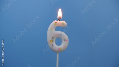 Burning white birthday candle on blue background, number 6.	