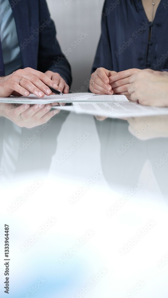 Unrecognizable business people are discussing a contract during meeting while sitting at the glass table in office, vertical close up view. Copy space area