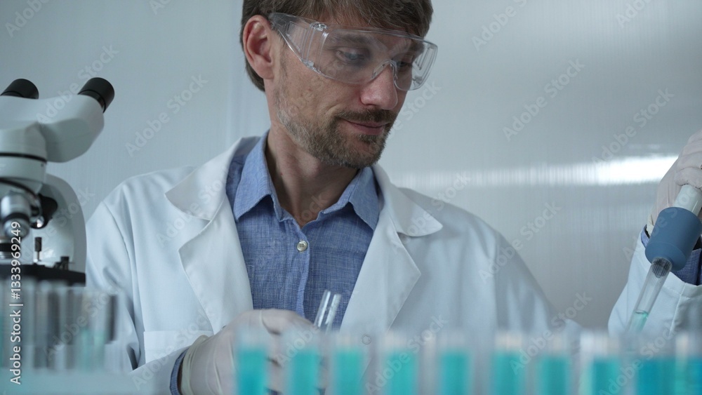 Scientist man wearing a lab coat and safety glasses is using a micropipette to drop a liquid into a test tube, portrait view. Medicine and science
