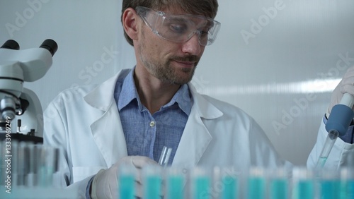 Obraz na płótnie Scientist man wearing a lab coat and safety glasses is using a micropipette to drop a liquid into a test tube, portrait view. Medicine and science w salonie