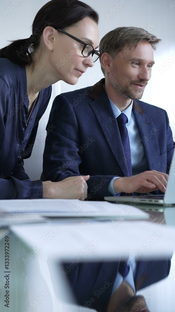 Two professionals collaborating in a modern office setting, using a laptop and discussing a project, vertical portrait. Business people concept