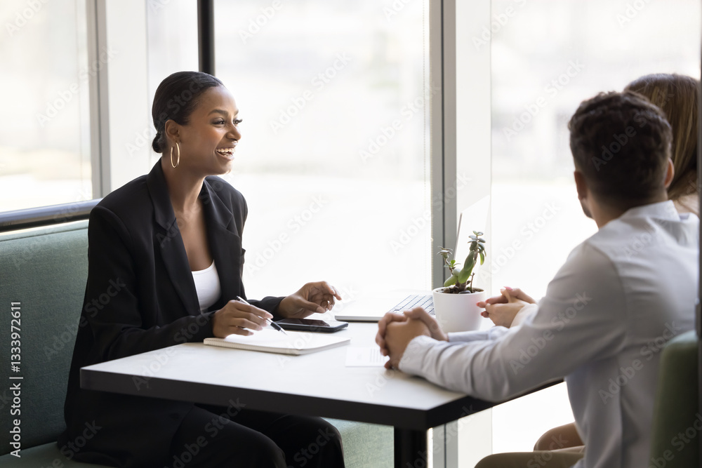 African professional woman leads negotiations with couple seated at table in office. Advisor or consultant explain contract details, share information about services, enjoy friendly talk with clients