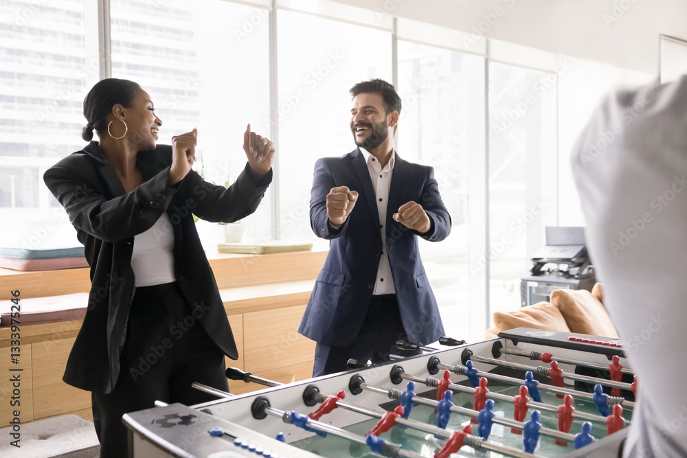 Fototapeta premium Two multiethnic colleagues winning foosball game, making dance-like gestures, joyfully celebrating moment of victory, feel overjoyed, enjoy funny teambuilding activity in modern office. Unity, spirit