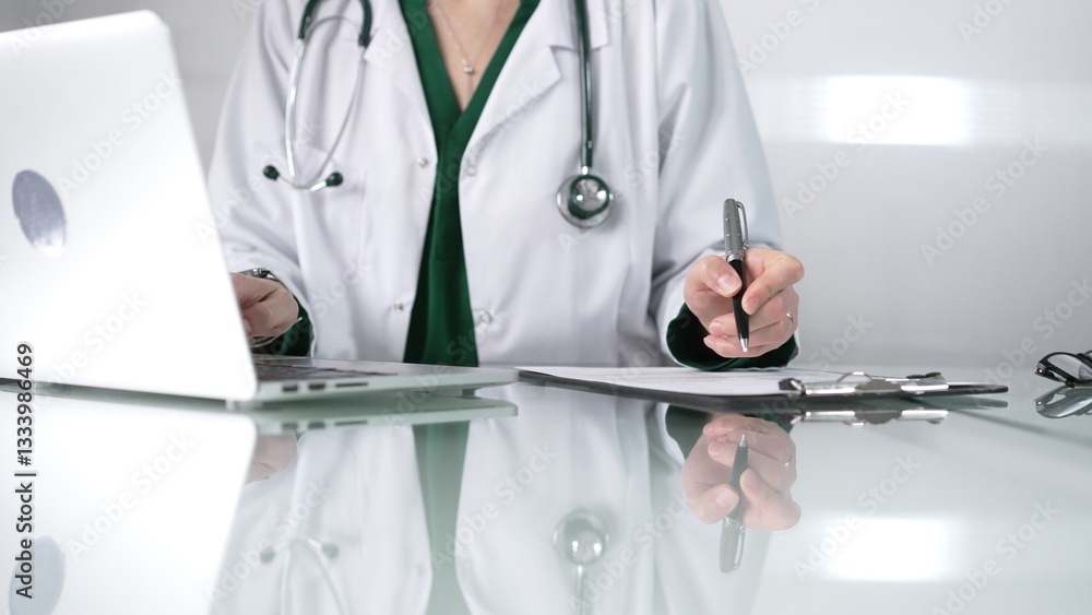 Woman doctor using a clipboard and taking notes on glass desk in a medical office, close-up view. Medicine concept