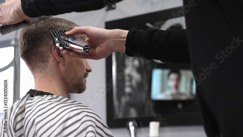 Professional barber trimming male client's hair using electric razor, creating precise haircut in contemporary barbershop setting with sleek styling tools