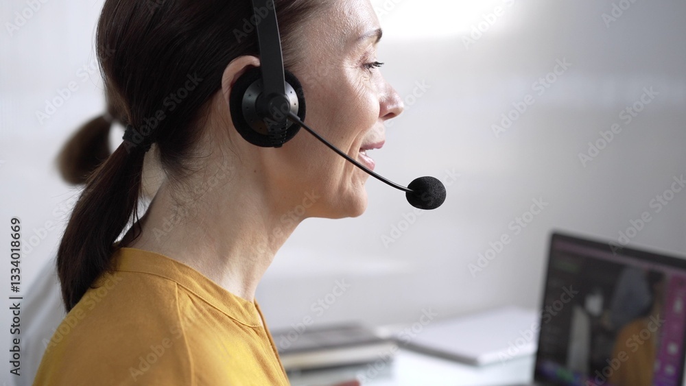 Focused female call center operator in yellow casual blouse is assisting clients online, providing customer support and answering inquiries. Call center concept