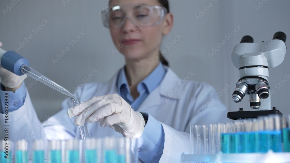 A scientist woman, wearing white gloves and safety glasses, is using a micropipette to drop a liquid into a test tubes. Medicine and science concept