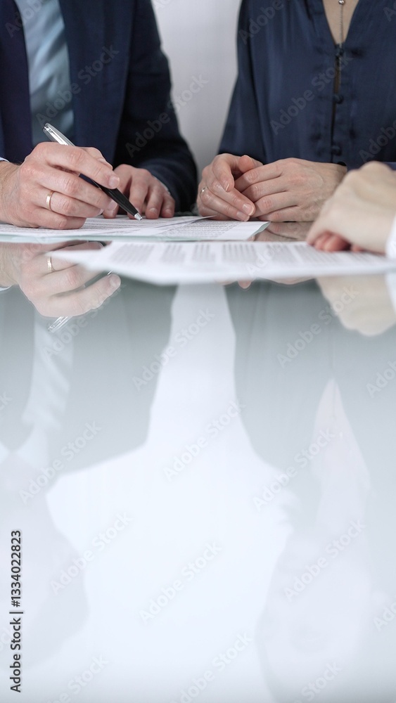 Unrecognizable business people are discussing a contract during meeting while sitting at the glass table in office, vertical close up view. Copy space area