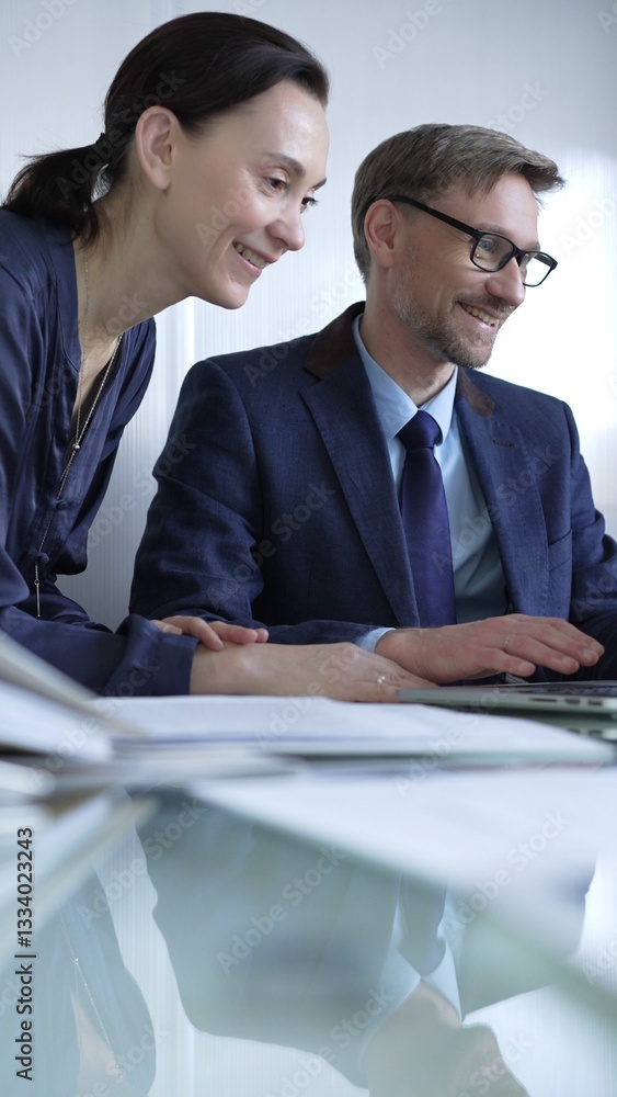 Two professionals collaborating in a modern office setting, using a laptop and discussing a project, vertical portrait. Business people concept