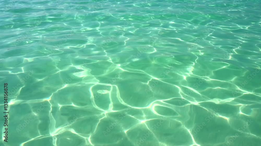 The surface of turquoise sea water glares under the rays of the sun. Sun glare at the bottom of the sea. Background ripple transparent water. The surface of turquoise sea water glares under the rays of the sun. Sun glare at the bottom of the sea. Background ripple transparent water.