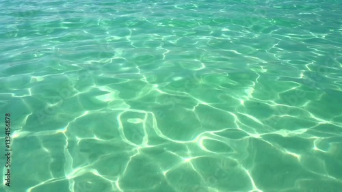 The surface of turquoise sea water glares under the rays of the sun. Sun glare at the bottom of the sea. Background ripple transparent water.