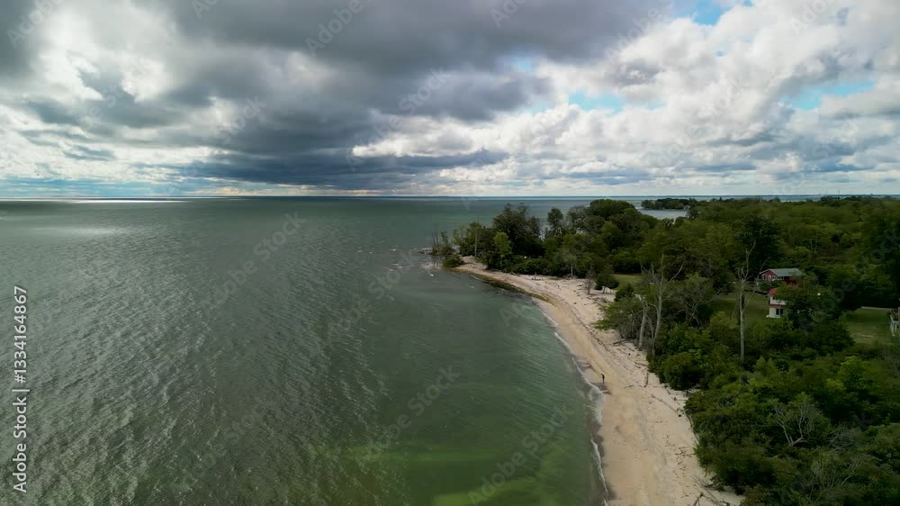 Aerial view of a sandy shoreline meeting calm waters, with a dense forest in the background and dramatic clouds overhead Aerial view of a sandy shoreline meeting calm waters, with a dense forest in the background and dramatic clouds overhead