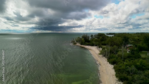 Wallpaper Mural Aerial view of a sandy shoreline meeting calm waters, with a dense forest in the background and dramatic clouds overhead Torontodigital.ca