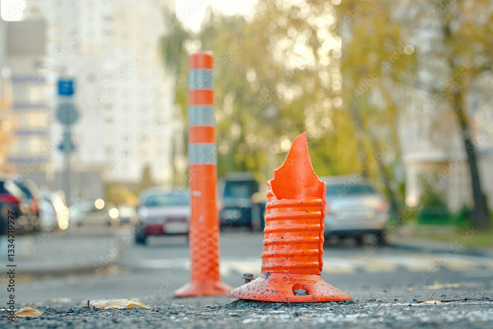 Broken and damaged orange traffic cone on an asphalt road, cracked and torn, serving as an ineffective anti-parking barrier that urgently needs replacement for safety. Selective focus