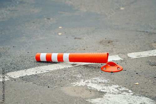 Damaged traffic cone lies knocked down on an asphalt road, cracked and torn, serving as an ineffective anti-parking barrier that urgently needs replacement for safety. Selective focus