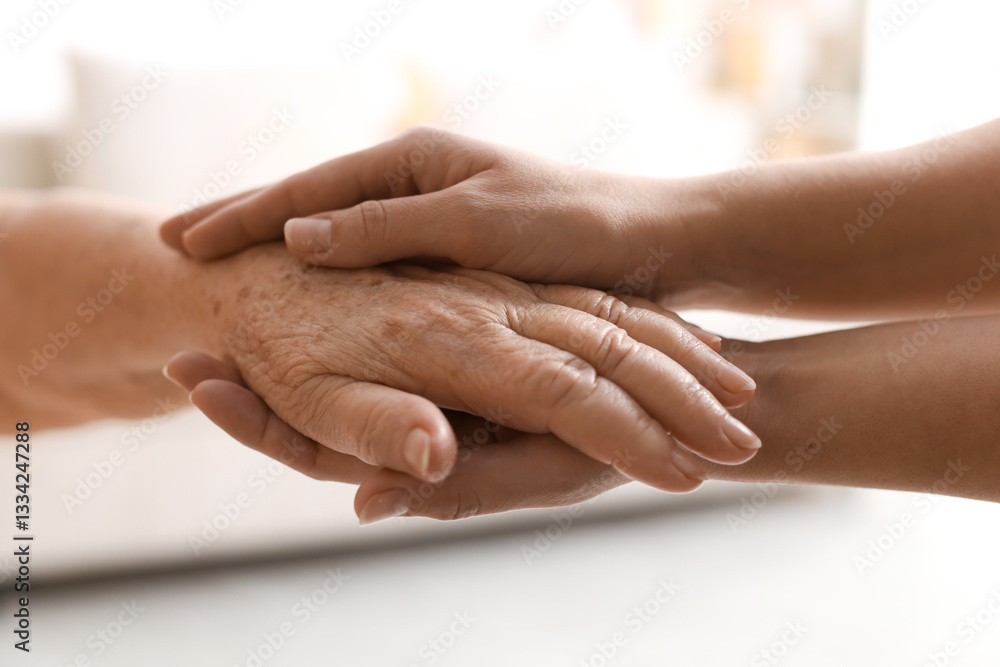 Fototapeta premium Caregiver supporting senior woman on light background, closeup. Elderly care