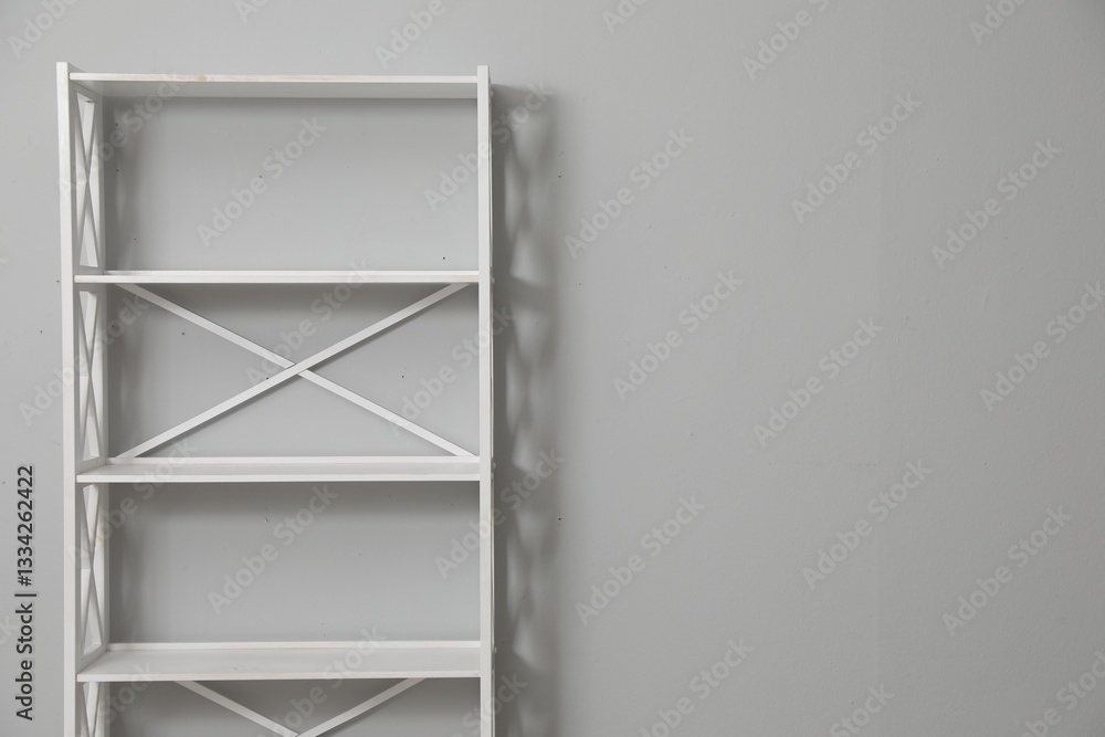 Empty shelving unit near light grey wall. Space for text Empty shelving unit near light grey wall. Space for text