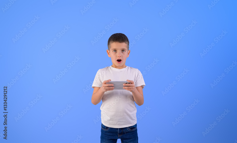 Portrait of shocked boy with mouth open playing video game over mobile phone against blue background Portrait of shocked boy with mouth open playing video game over mobile phone against blue background