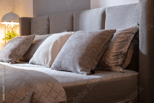 Vertical shot of bedroom interior with modern reading lamp on bedside table close to double bed with pillow. Evening light in cozy apartment