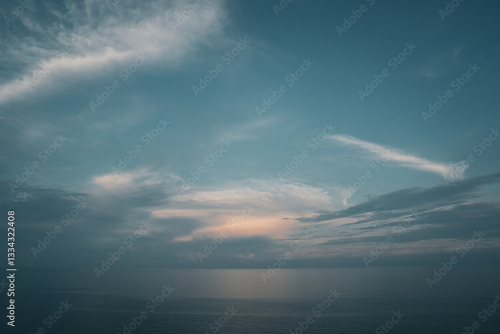 Obraz premium The blue sky in the early morning meets the calm, serene ocean, creating a tranquil, peaceful view. Soft light at dawn paints the horizon, making the sunrise an atmospheric, scenic skyscape of nature.