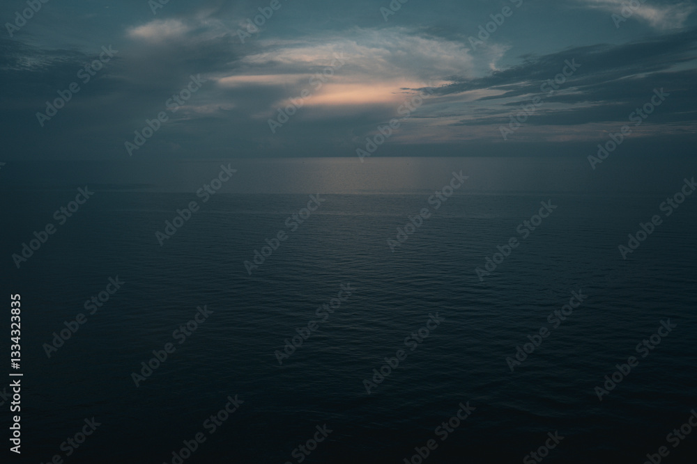 Obraz premium The blue sky in the early morning meets the calm, serene ocean, creating a tranquil, peaceful view. Soft light at dawn paints the horizon, making the sunrise an atmospheric, scenic skyscape of nature.