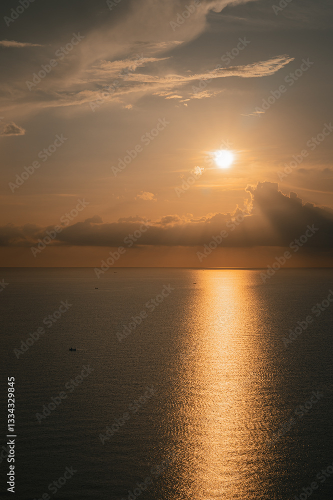 Naklejka premium In the early morning, the golden sky glows as the sunrise paints the ocean in warm hues. Golden water shimmers with sunlight on waves, creating a breathtaking and peaceful start to the day.