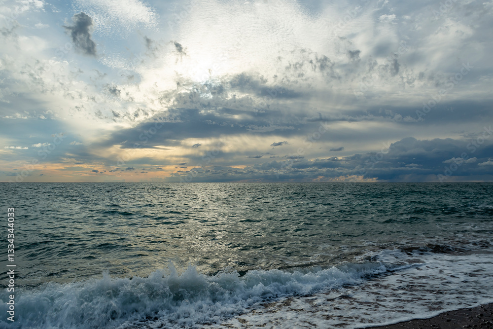 The sound of sea waves crashing on a pebble beach. The setting sun hid behind dark clouds. The sound of sea waves crashing on a pebble beach. The setting sun hid behind dark clouds.