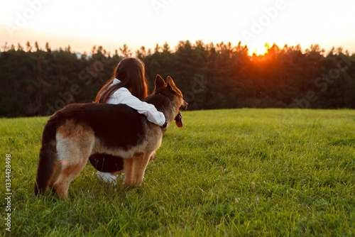 Young woman embracing her german shepherd dog while enjoying a peaceful moment in a meadow at sunset, creating a heartwarming scene of companionship and tranquility