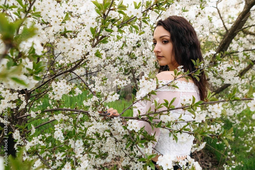 Beautiful brunette woman with long hair wearing white lace blouse posing near blooming cherry tree in spring garden, enjoying the pleasant warm weather Beautiful brunette woman with long hair wearing white lace blouse posing near blooming cherry tree in spring garden, enjoying the pleasant warm weather