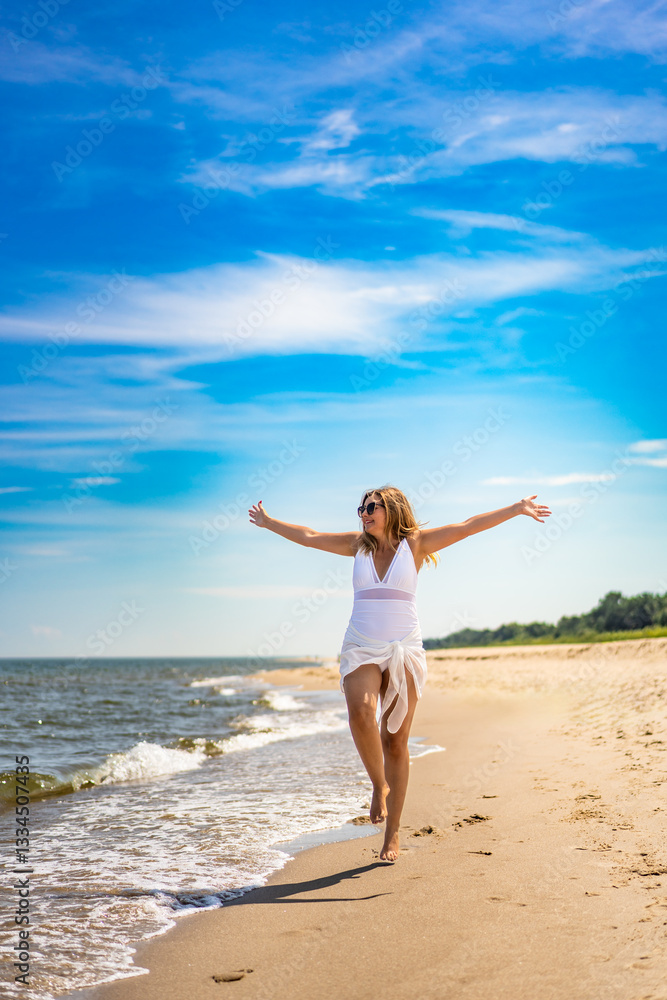 Beautiful middle-aged woman in swimsuit walking with outstretched arms on sandy beach in summertime. Energy and happiness. Front view Beautiful middle-aged woman in swimsuit walking with outstretched arms on sandy beach in summertime. Energy and happiness. Front view