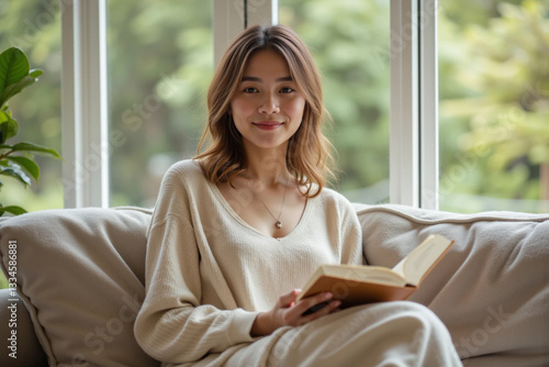 Charming Millennial Woman in Short Skirt Reading a Book on Sofa by Large Window – Cozy and Relaxed Moment
 photo