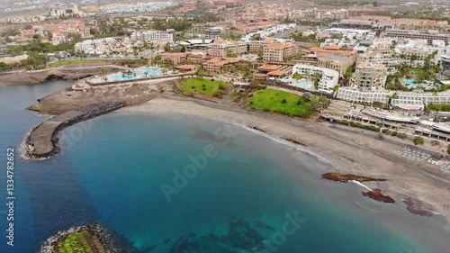 Aerial view of Costa Adeje city beach, Tenerife, Canary islands. Cinematic 4K footage with sandy coast, clear turquoise waters of Atlantic ocean, villas, resorts, quay. Dynamic rising moving shot 