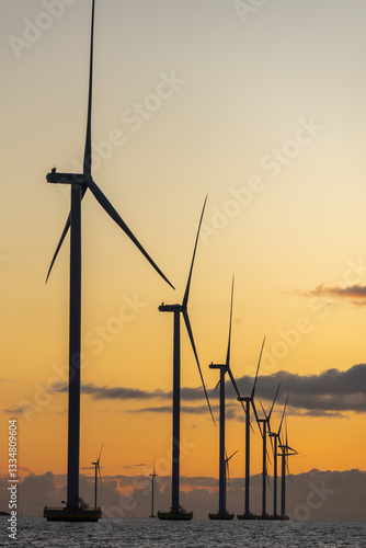 Row of offshore wind turbines against orange sunset sky in Netherlands