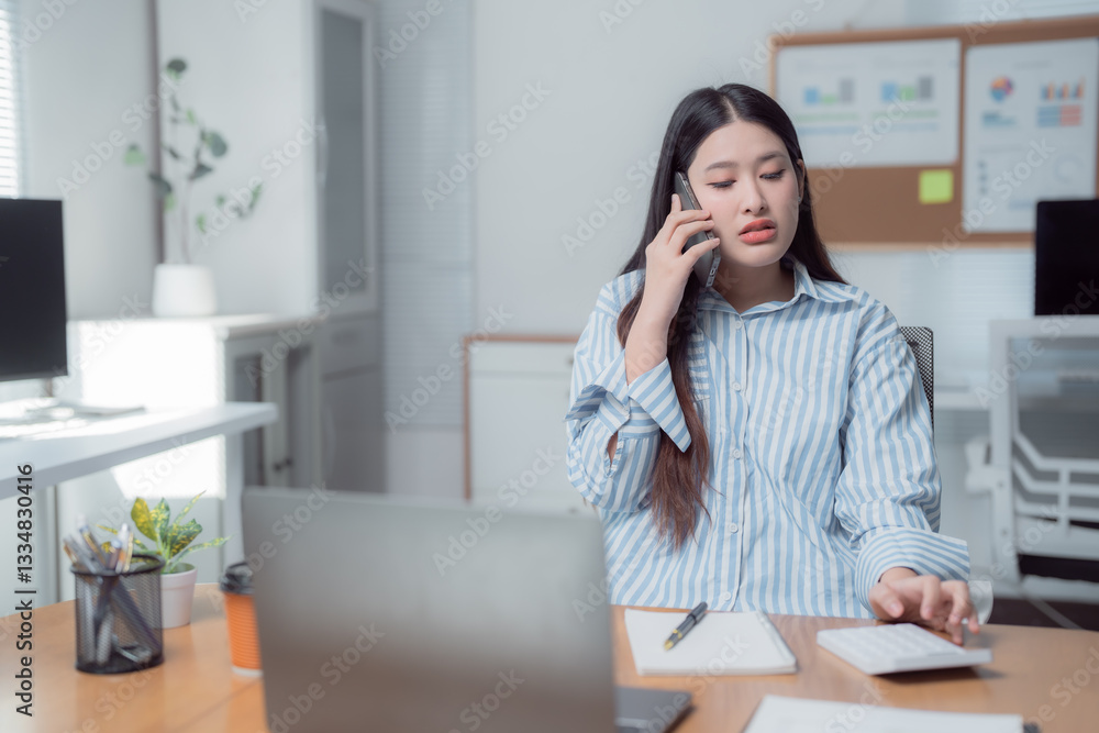 Businesswoman managing her office tasks, using a calculator and talking on the phone while working at her desk. Engaging in finance and communication in a modern, organized workspace Businesswoman managing her office tasks, using a calculator and talking on the phone while working at her desk. Engaging in finance and communication in a modern, organized workspace