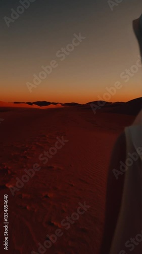 a girl walks through the desert at sunset wearing a veil.
