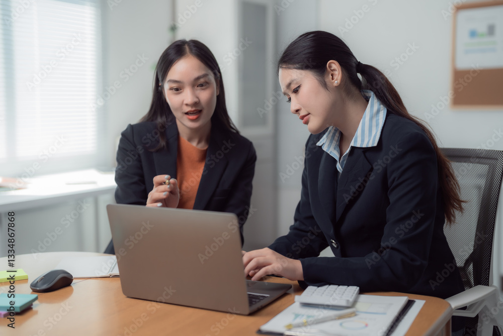 Two Asian businesswomen collaborating in a modern office, working together on a laptop while discussing and analyzing financial graphs alongside the company budget Two Asian businesswomen collaborating in a modern office, working together on a laptop while discussing and analyzing financial graphs alongside the company budget