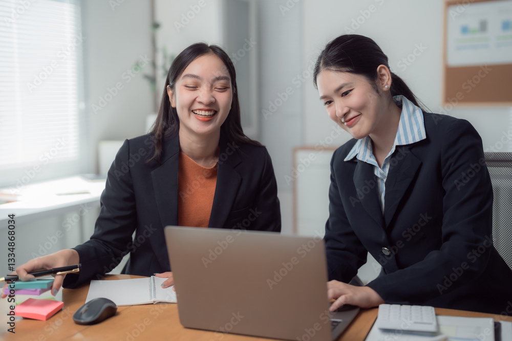 Two asian businesswomen are smiling and collaborating on a project, using a laptop in a bright and modern office environment, showcasing teamwork and productivity Two asian businesswomen are smiling and collaborating on a project, using a laptop in a bright and modern office environment, showcasing teamwork and productivity